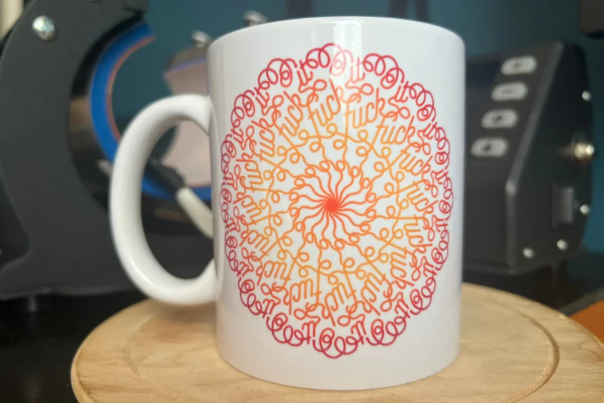 Fehér bögre színes mandaladizájnnal, amiben apró betűkkel a "fuck" szó ismétlődik körkörösen.