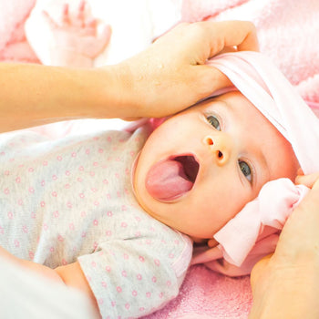 Baba termékek kisbabáknak: előke, cumi, takaró és puha játék egy babaszobában, gondosan elrendezve, biztonságos és kényelmes környezetben.